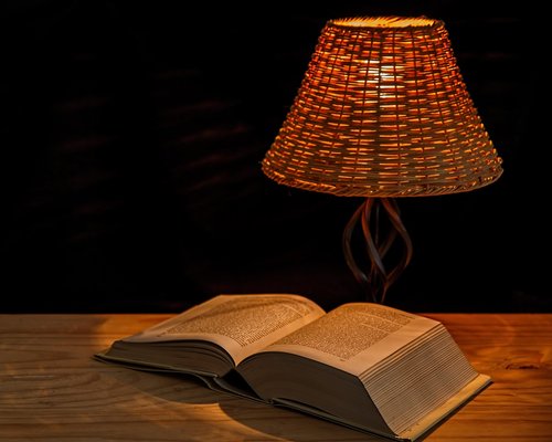 Hands holding a physical book under the soft light of a reading lamp